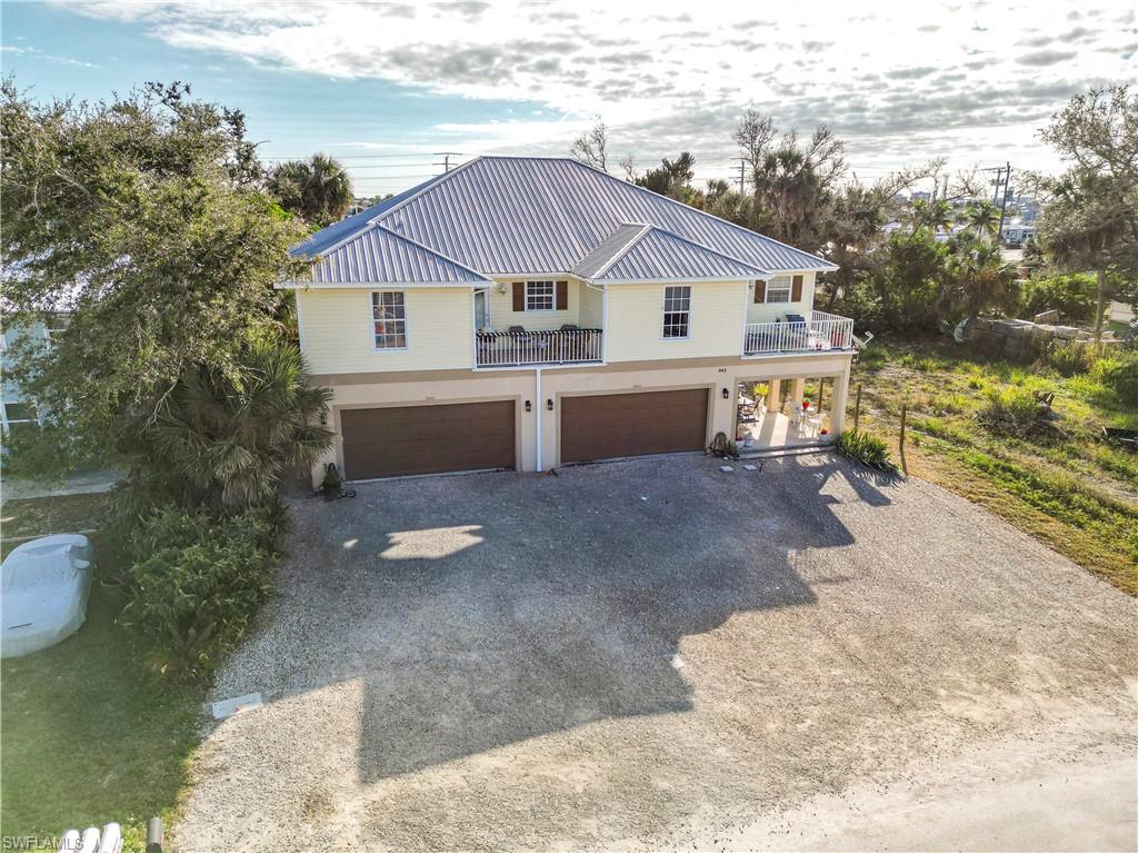 Coastal inspired home with gravel driveway, a balcony, a metal roof, and an attached garage