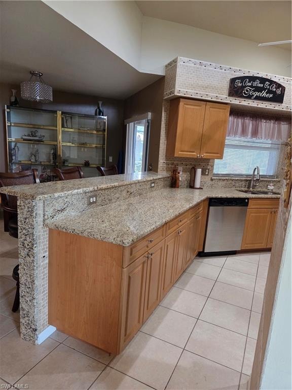 Kitchen with light tile floors, granite stone counters, dishwashing machine, a breakfast bar peninsula.