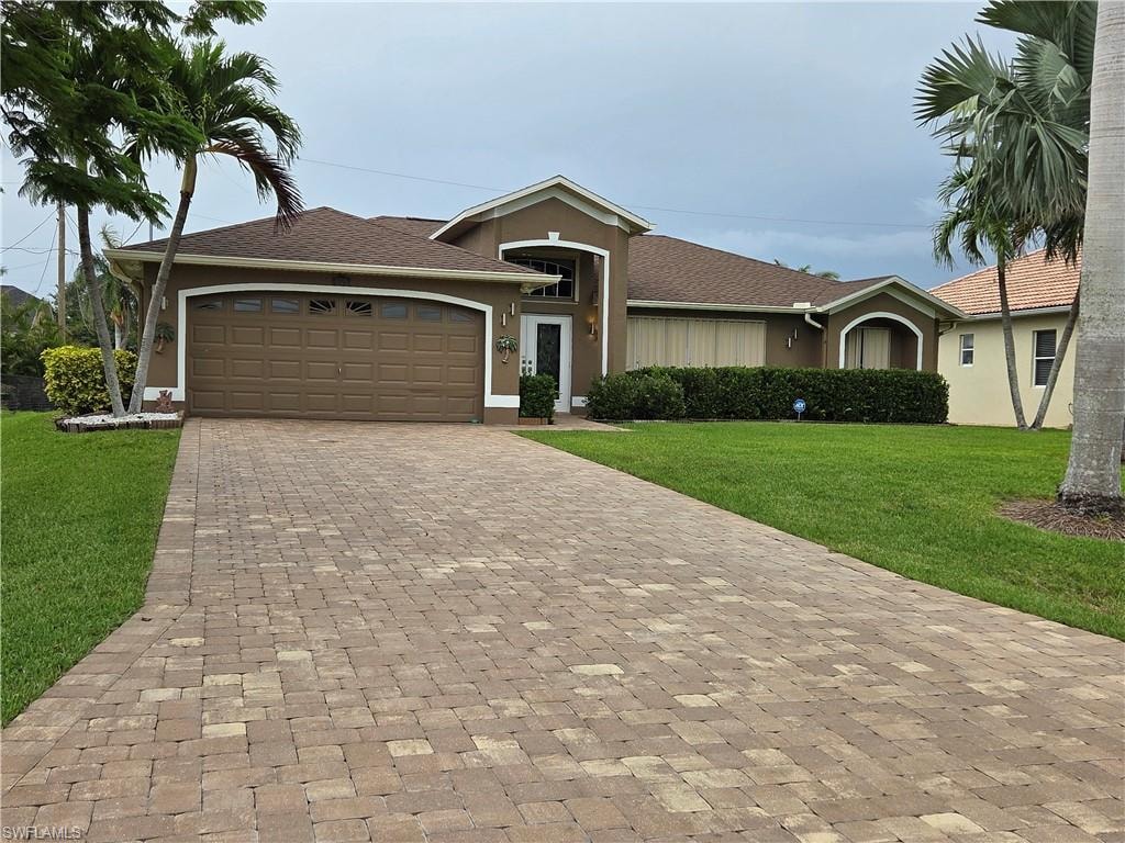 Ranch-style home featuring a front lawn, stucco siding, paver driveway, and a 2 car garage