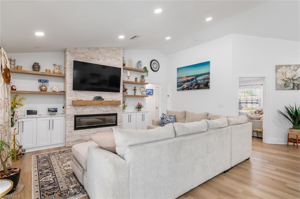 Living room with lofted ceiling, a large fireplace, light wood-style floors, and recessed lighting