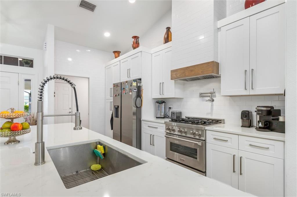 Kitchen featuring stainless steel appliances, white cabinets, light stone counters, premium range hood, and recessed lighting