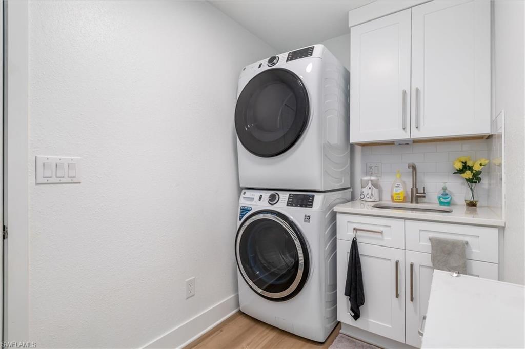 Washroom with estacked washer and dryer, cabinet space, and light wood finished floors
