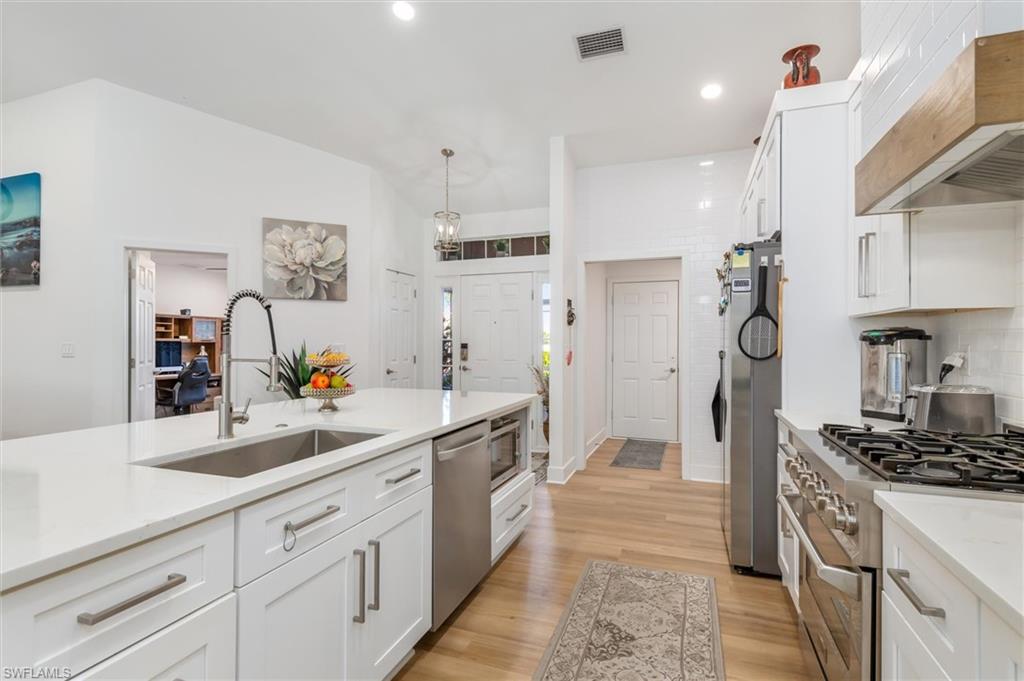 Kitchen with white cabinets, appliances with stainless steel finishes, hanging light fixtures, premium range hood, and light wood-type flooring