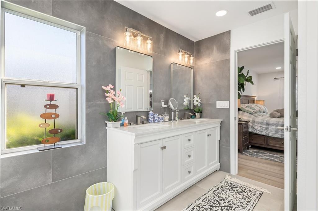 Full bathroom with double vanity, connected bathroom, tile walls, and recessed lighting