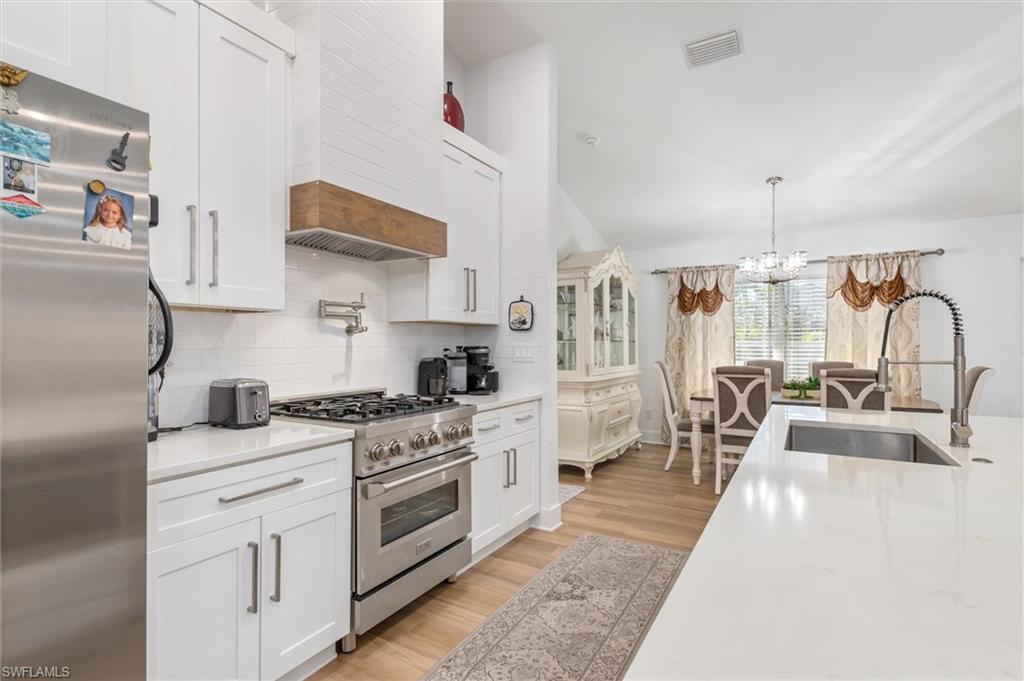 Kitchen featuring appliances with stainless steel finishes, white cabinetry, a chandelier, decorative light fixtures, and light stone counters