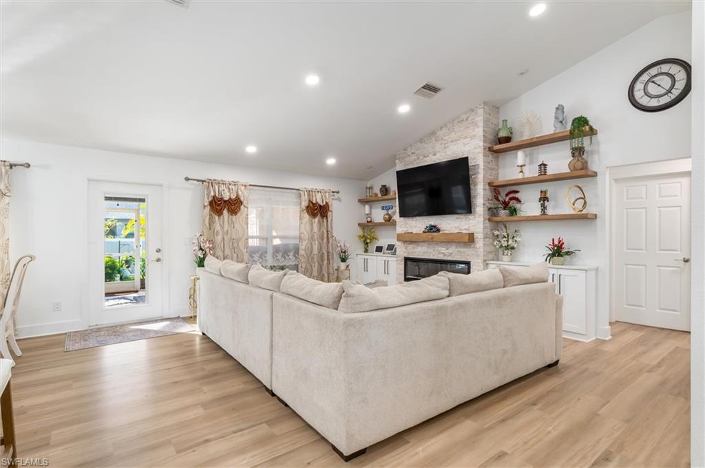 Living room featuring a fireplace, light wood-type flooring, recessed lighting, and high vaulted ceiling
