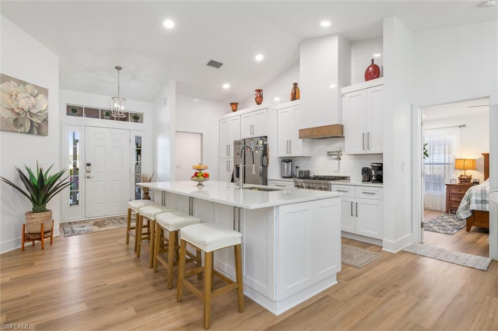 Kitchen with white cabinets, decorative light fixtures, a breakfast bar, an island with sink, and light wood finished floors
