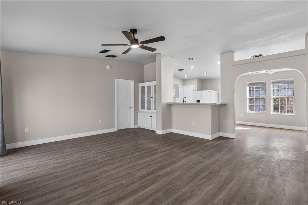 Unfurnished living room featuring a ceiling fan, arched walkways, dark wood-type flooring, and recessed lighting