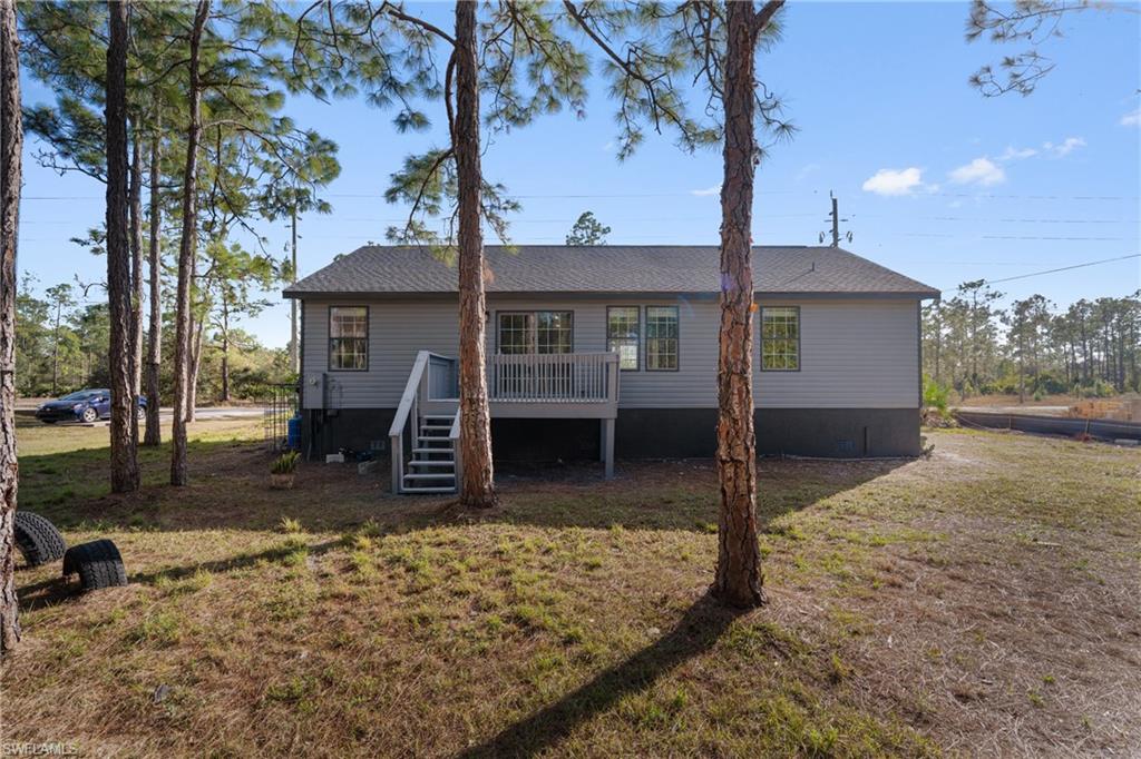 Back of property with a wooden deck, a lawn, stairs, and roof with shingles