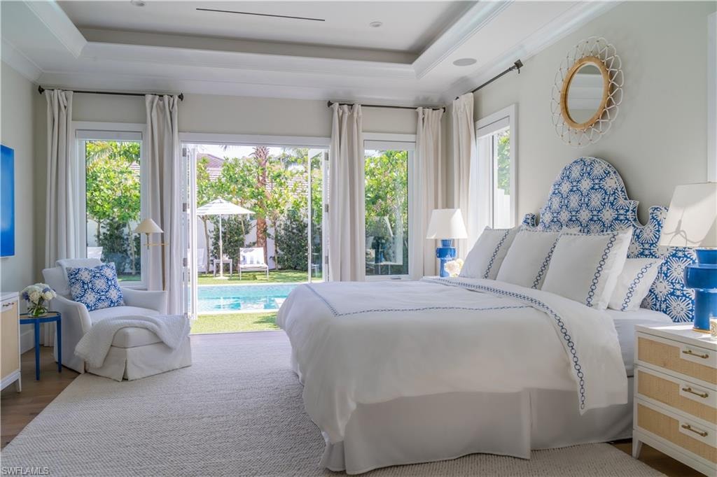 Bedroom with multiple windows, access to exterior, a raised ceiling, wood finished floors, and ornamental molding