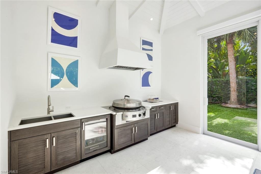 Bar area featuring dark brown cabinetry, wall chimney range hood, stainless steel cooktop, modern cabinets, and wine cooler