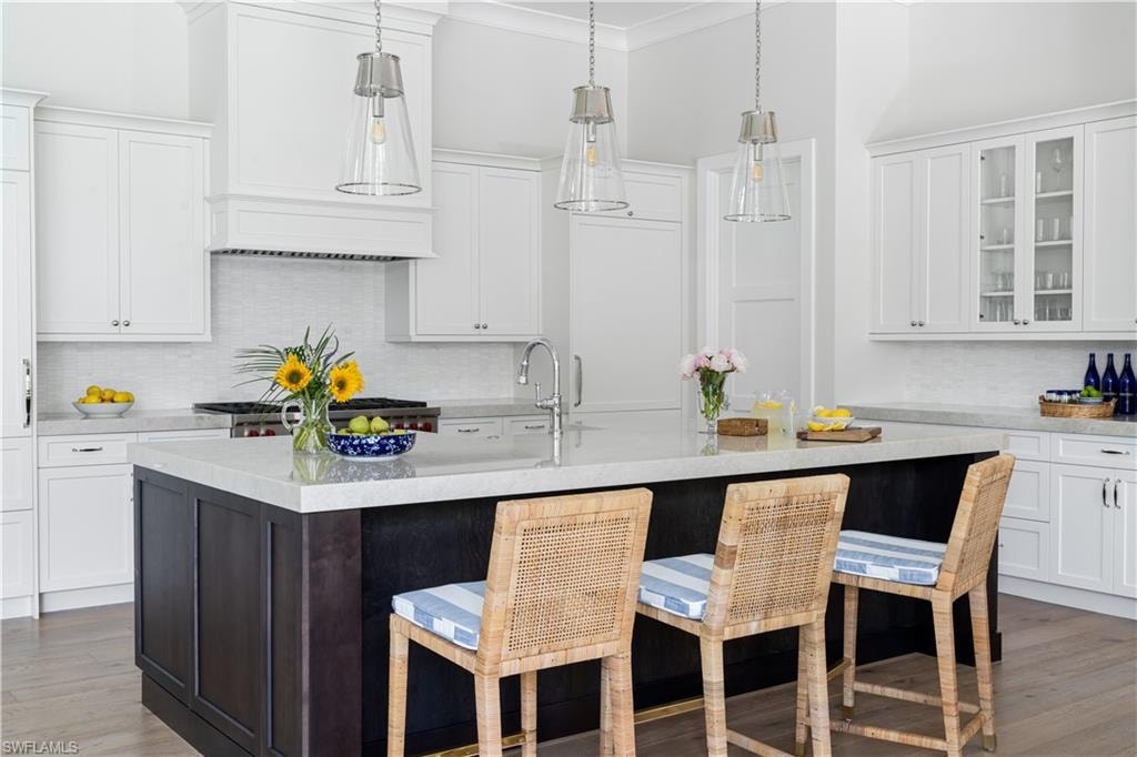 Kitchen with decorative backsplash, white cabinetry, light wood-style flooring, decorative light fixtures, and ornamental molding