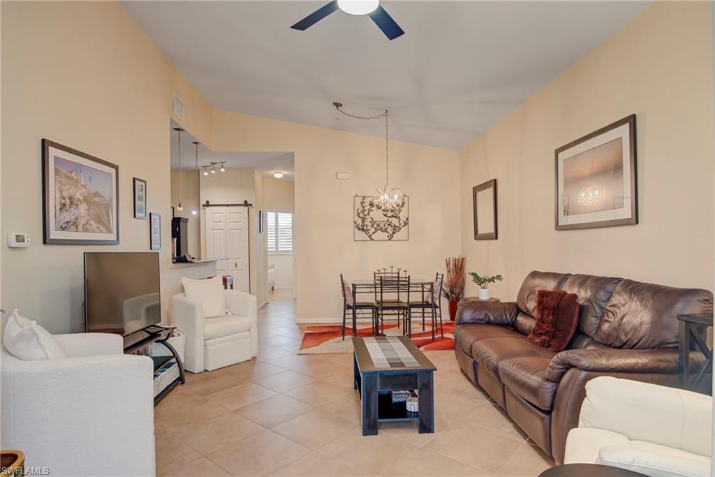 Living area with light tile patterned floors, vaulted ceiling, a chandelier, and a ceiling fan