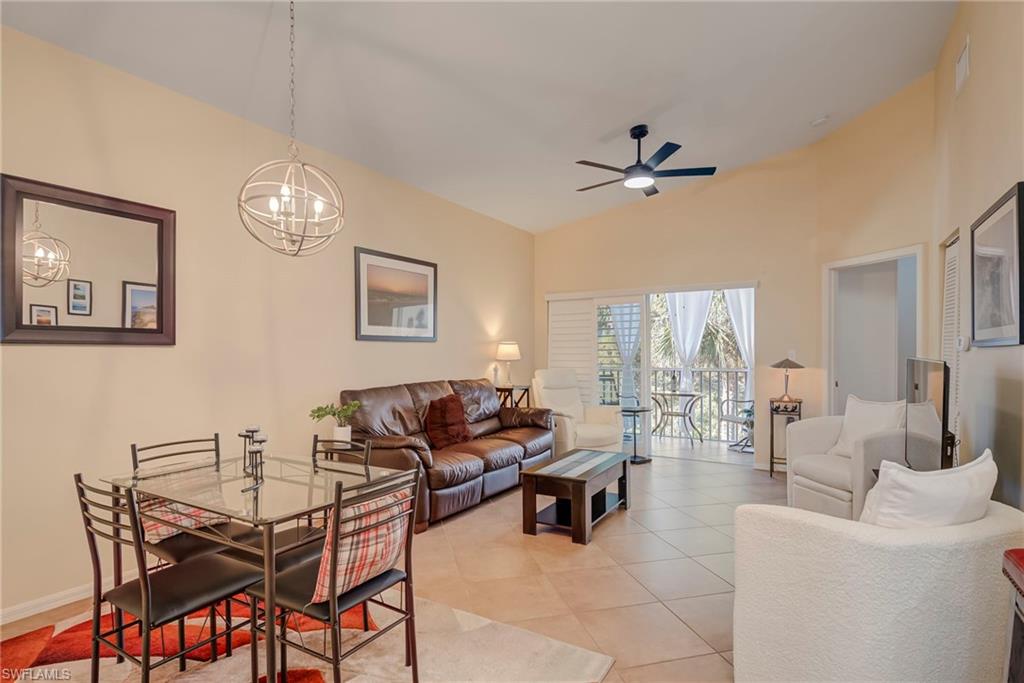Living room with lofted ceiling, light tile patterned floors, ceiling fan, and a chandelier