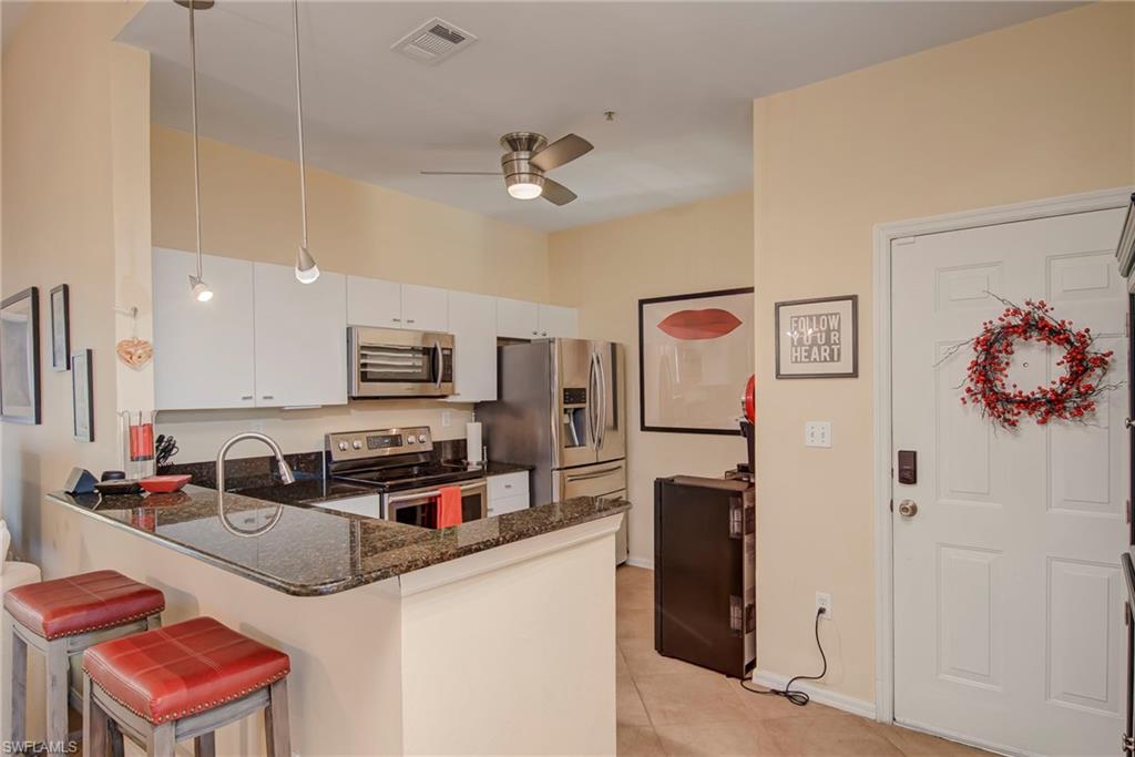 Kitchen featuring stainless steel appliances, dark stone countertops, decorative light fixtures, white cabinetry, and a peninsula