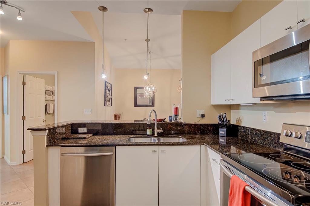 Kitchen with appliances with stainless steel finishes, white cabinetry, dark stone counters, and hanging light fixtures