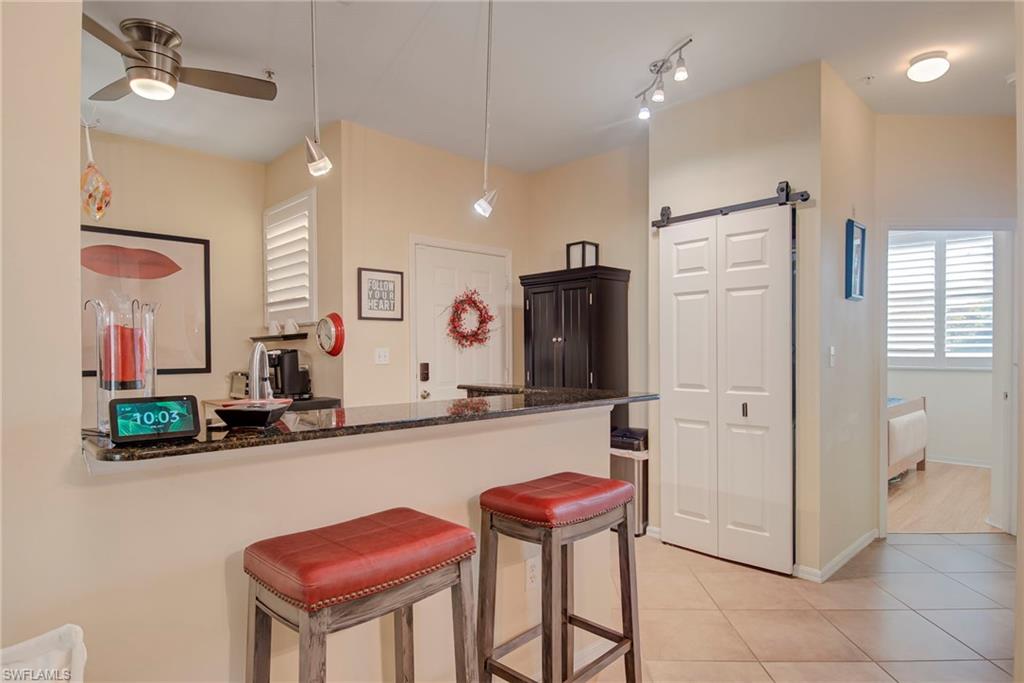 Kitchen featuring a barn door, a breakfast bar area, decorative light fixtures, light tile patterned floors, and dark stone countertops