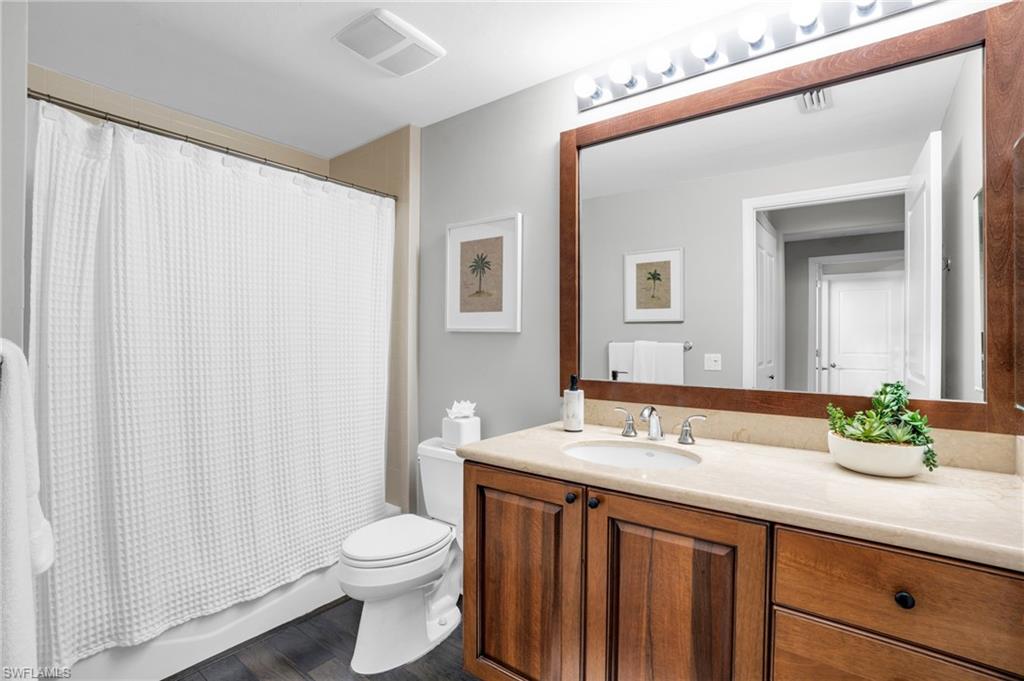 Full bathroom featuring shower / tub combo with curtain, vanity, and dark wood-style floors