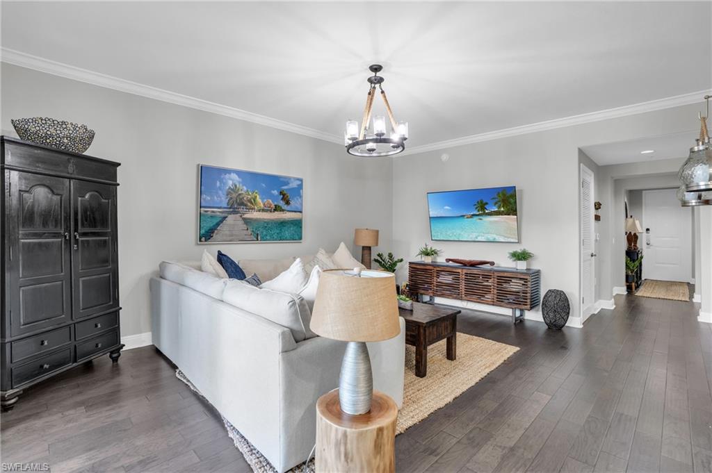 Living room with dark wood finished floors, crown molding, and a chandelier