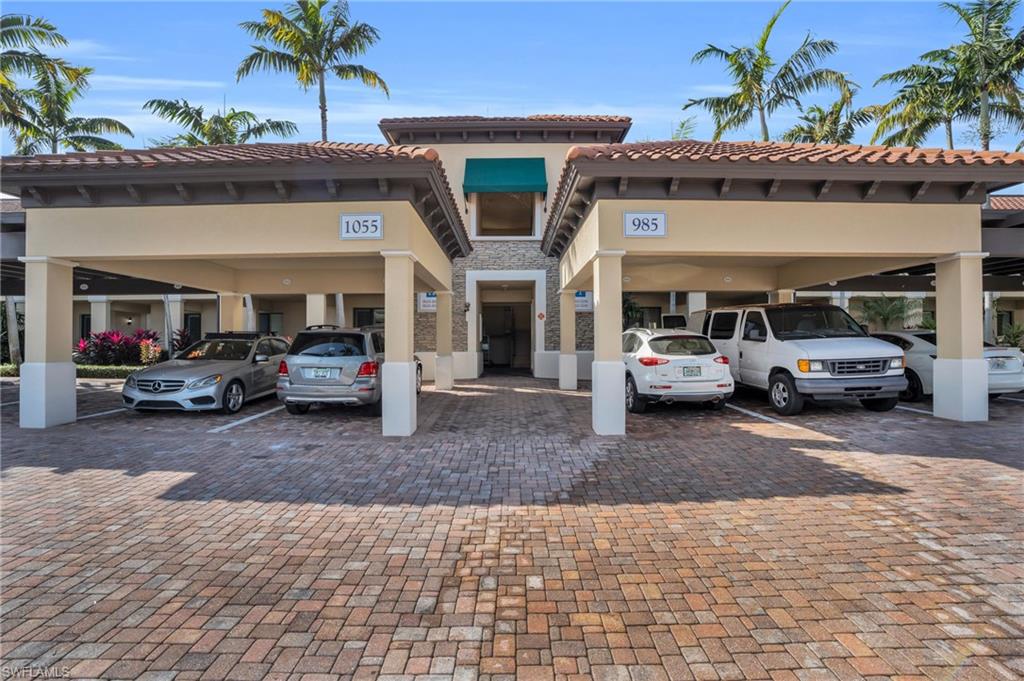 View front of complex with a tiled roof, stucco siding, stone siding, and covered parking