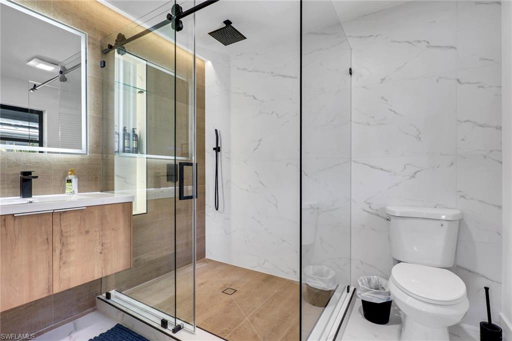 Bathroom featuring Bathroom-vanity, a marble finish shower, and tile walls