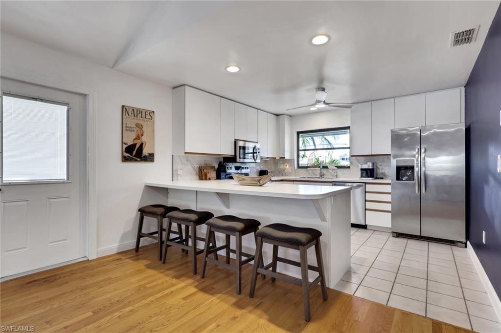 Kitchen with appliances with stainless steel finishes, a breakfast bar, light countertops, white cabinetry, and recessed lighting