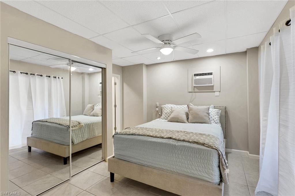 1/1 Efficiency-Bedroom featuring a paneled ceiling, light tile patterned floors, ceiling fan, a closet, and a wall mounted AC