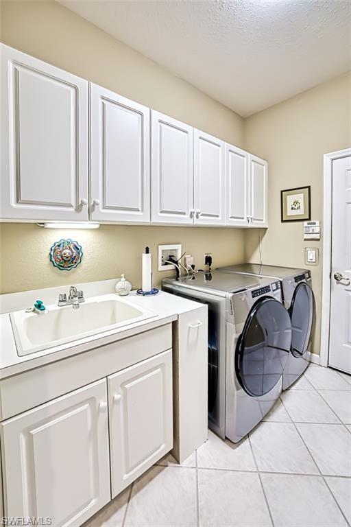 Washroom featuring light tile patterned flooring, a textured ceiling, cabinet space, and washer and dryer