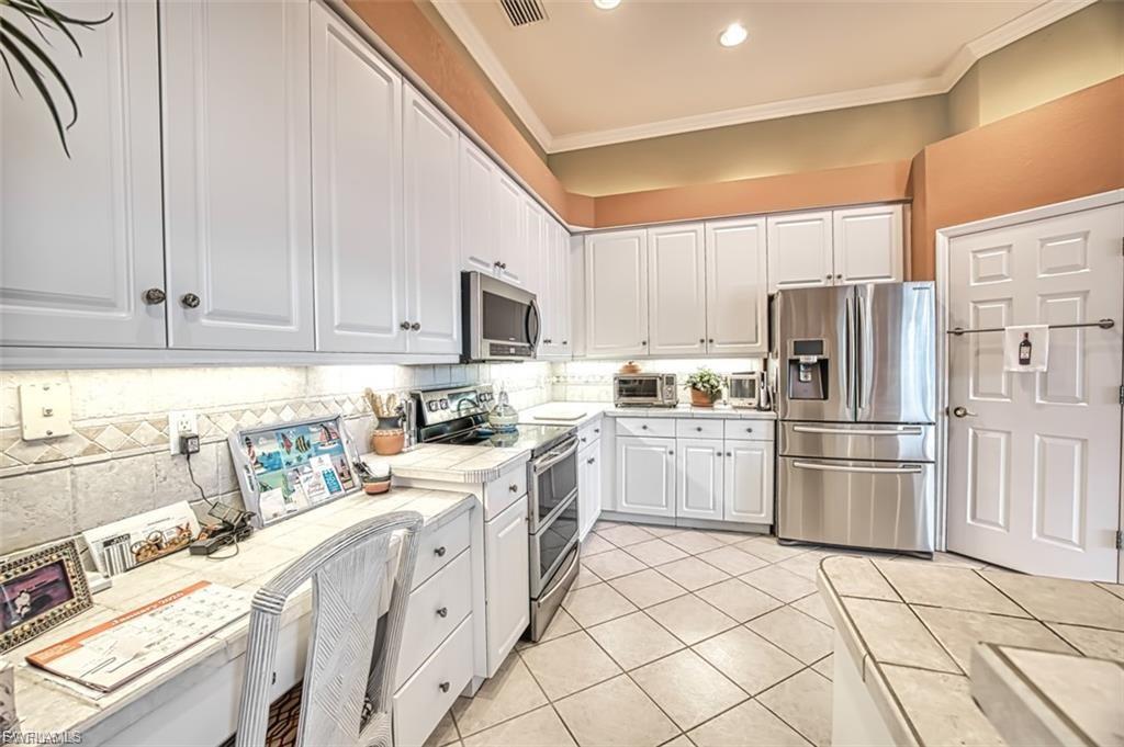Kitchen featuring appliances with stainless steel finishes, white cabinets, tile countertops, light tile patterned flooring, and crown molding