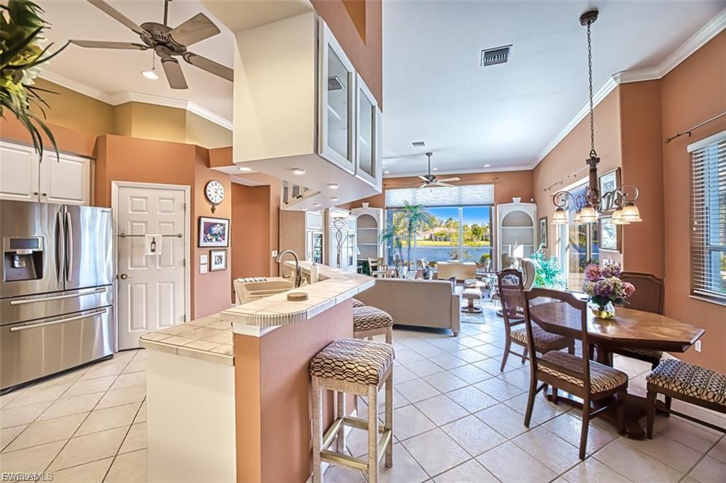 Kitchen featuring a ceiling fan, stainless steel refrigerator with ice dispenser, crown molding, light tile patterned floors, and tile counters