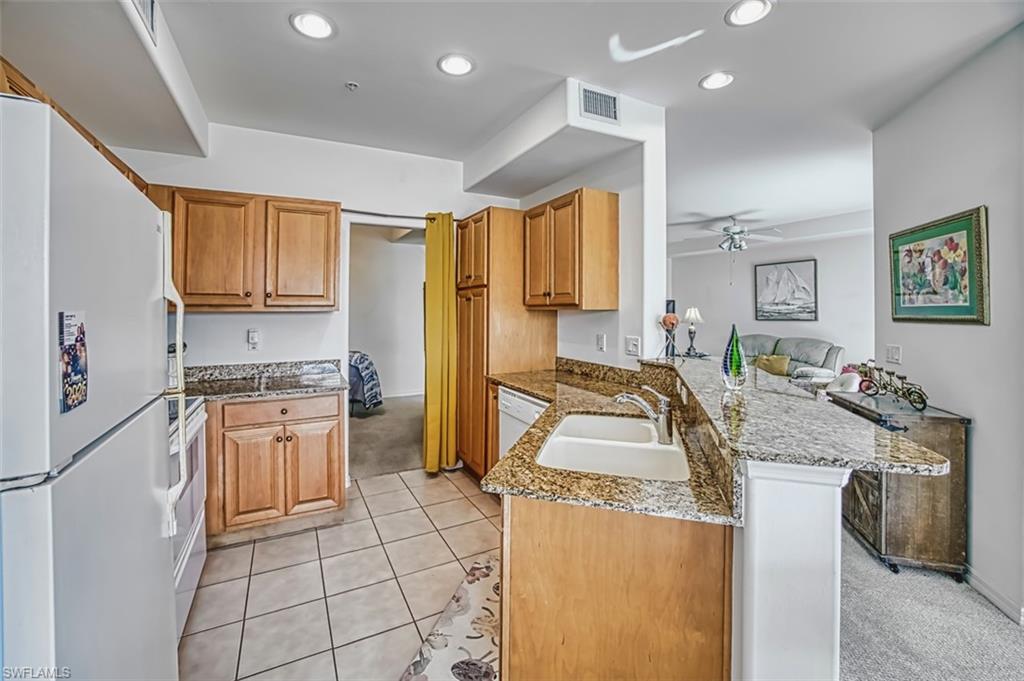 Kitchen featuring white appliances, light stone counters, brown cabinetry, a peninsula, and a ceiling fan
