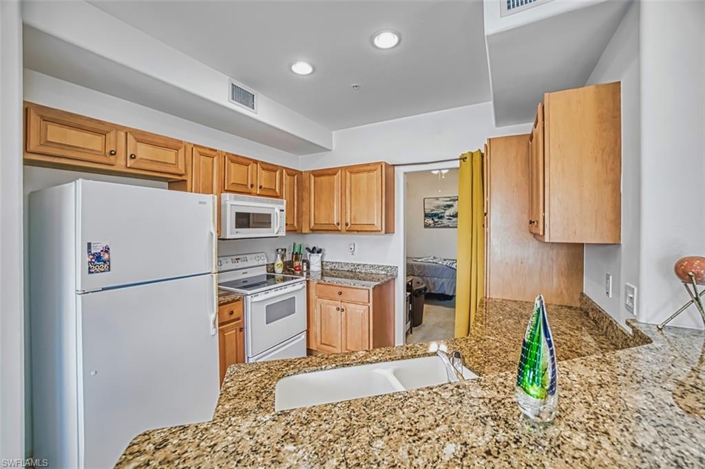 Kitchen with white appliances, light stone countertops, recessed lighting, and brown cabinets