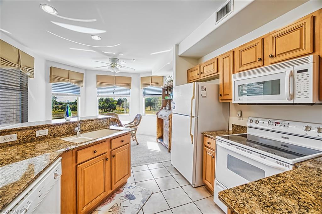 Kitchen with white appliances, dark stone countertops, light tile patterned floors, a ceiling fan, and brown cabinets