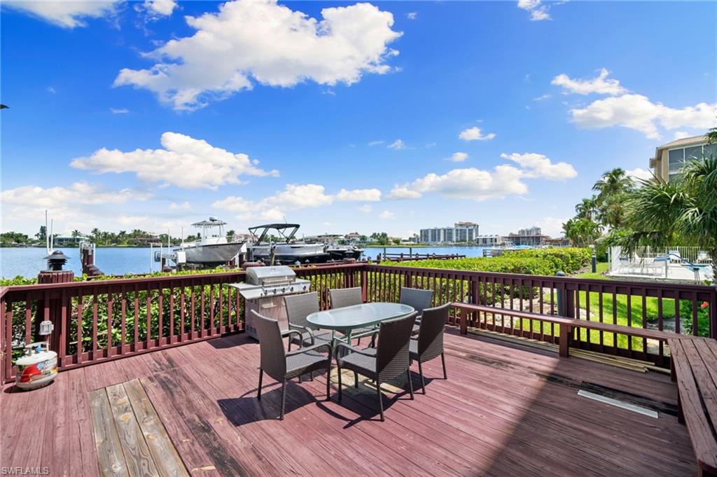 Wooden deck with outdoor dining area, a water view, and a grill