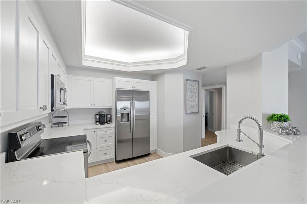Kitchen with appliances with stainless steel finishes, light wood-style flooring, white cabinets, and light stone counters