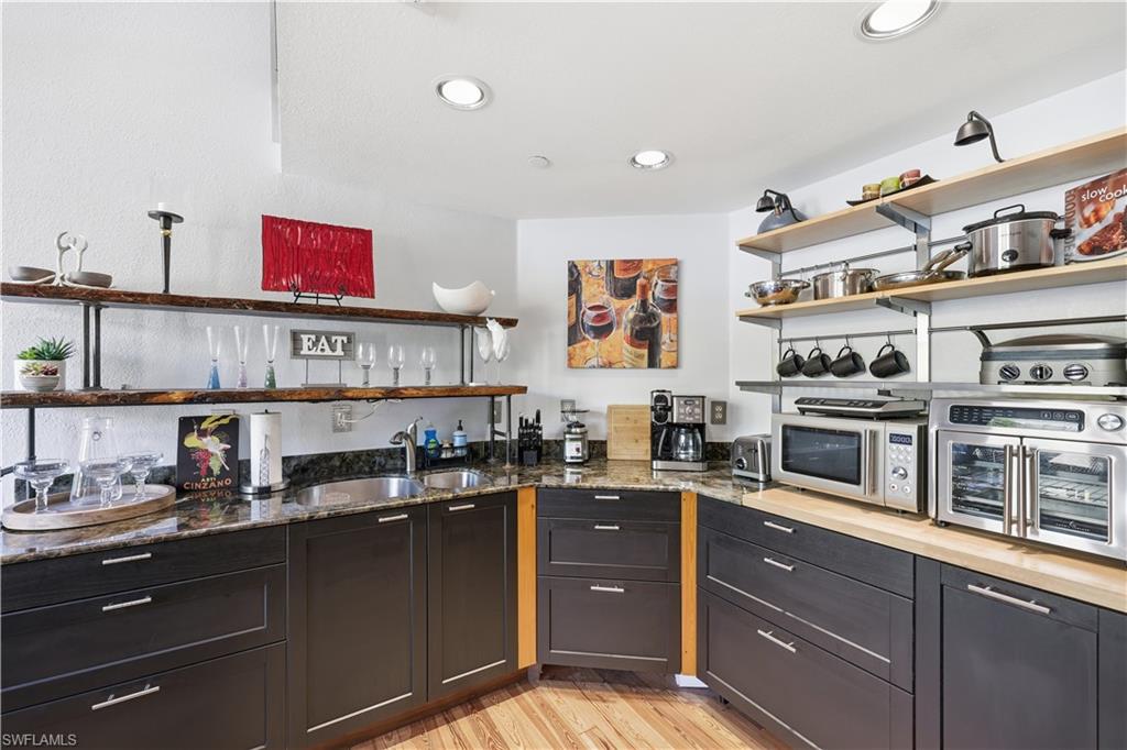 Kitchen with open shelves, light wood-style flooring, dark stone countertops, recessed lighting, and stainless steel microwave