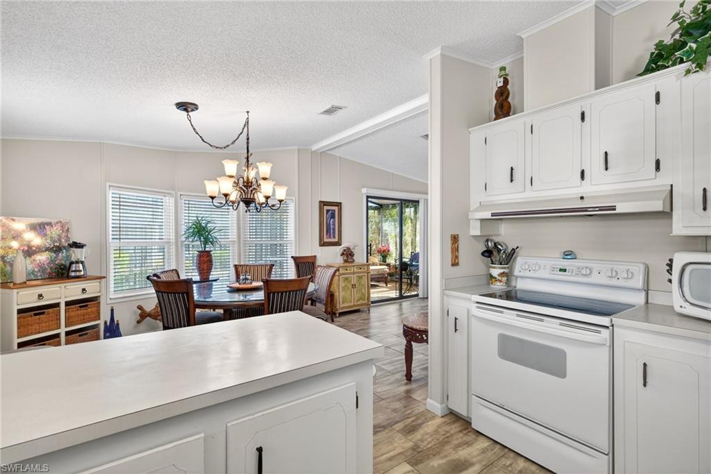 Kitchen featuring white appliances, white cabinets, light countertops, a chandelier, and lofted ceiling