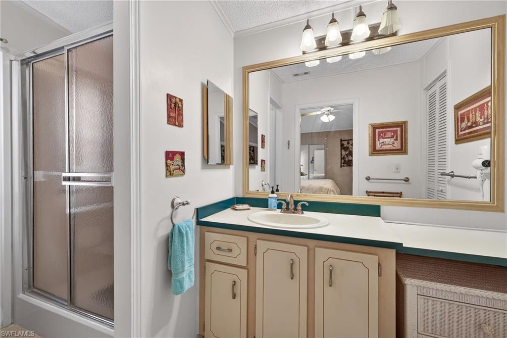 Ensuite bathroom featuring vanity, a textured ceiling, a stall shower, ceiling fan, and crown molding