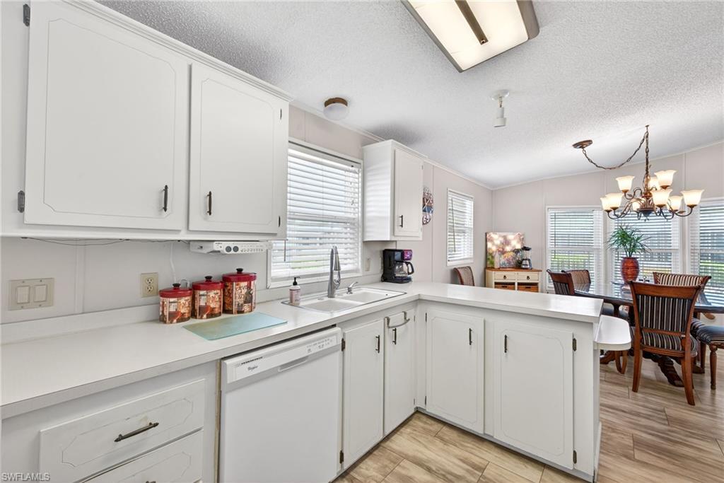 Kitchen with a peninsula, light countertops, dishwasher, white cabinets, and a chandelier