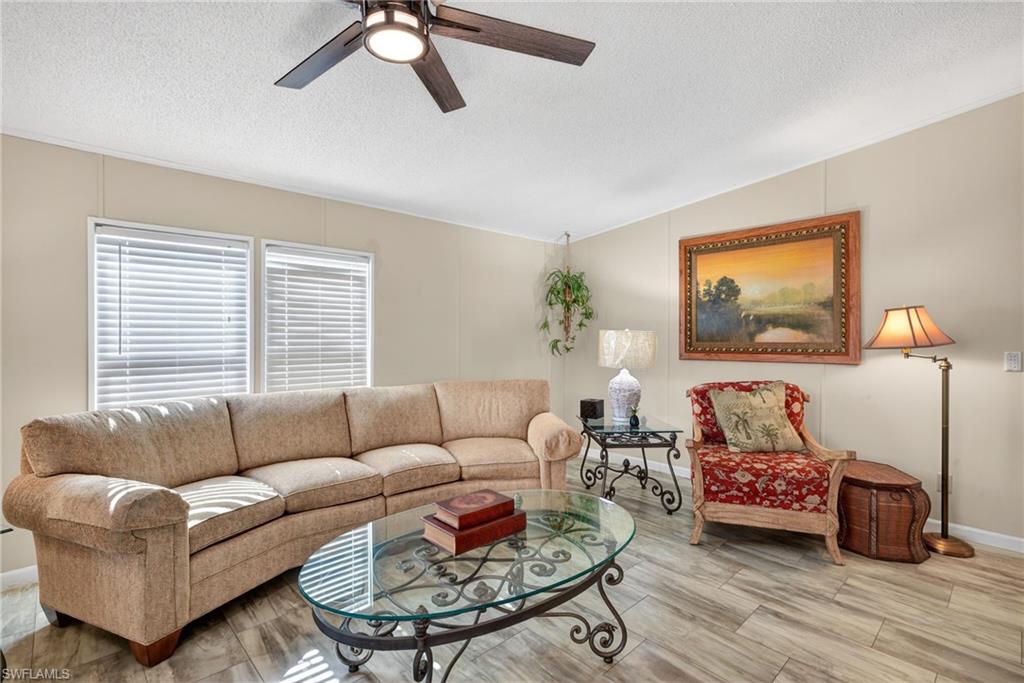 Living room with a textured ceiling, wood finished floors, a ceiling fan, and a decorative wall