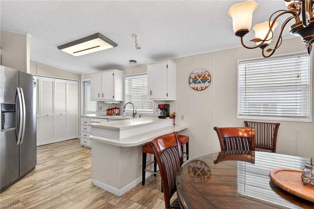 Kitchen with a peninsula, stainless steel fridge with ice dispenser, light countertops, a kitchen breakfast bar, and a textured ceiling