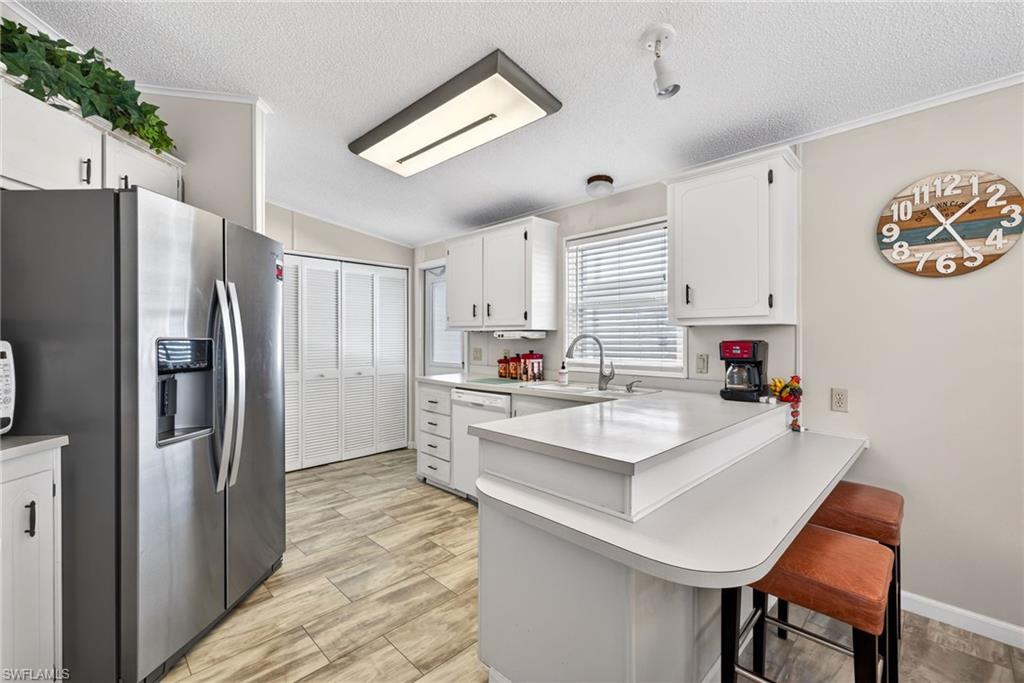 Kitchen featuring stainless steel fridge, light countertops, white cabinets, a breakfast bar, and a peninsula