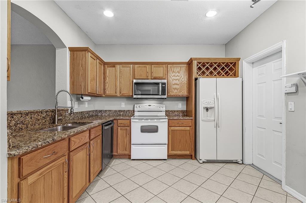 Kitchen with dark stone counters, appliances with stainless steel finishes, brown cabinets, arched walkways, and recessed lighting