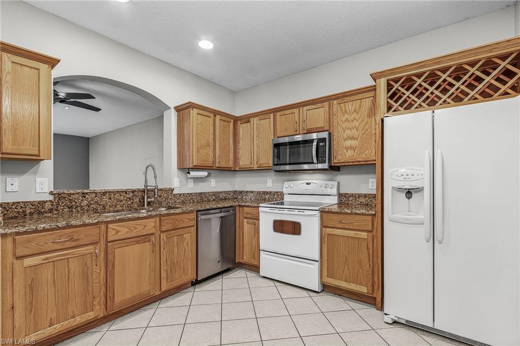 Kitchen featuring stainless steel appliances, dark stone countertops, ceiling fan, arched walkways, and brown cabinetry