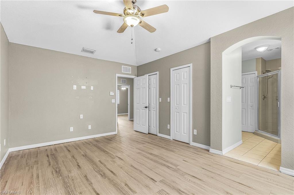 Unfurnished bedroom with multiple closets, light wood-type flooring, arched walkways, ensuite bath, and ceiling fan