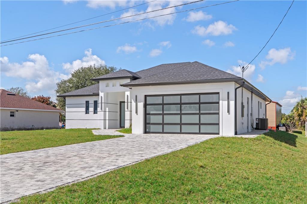View of front of property with a front yard, decorative driveway, stucco siding, and roof with shingles