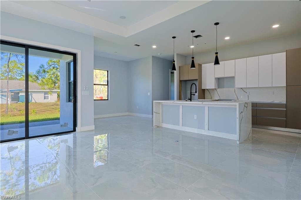 Kitchen featuring modern cabinets, white cabinets, a kitchen island with sink, decorative light fixtures, and light stone counters