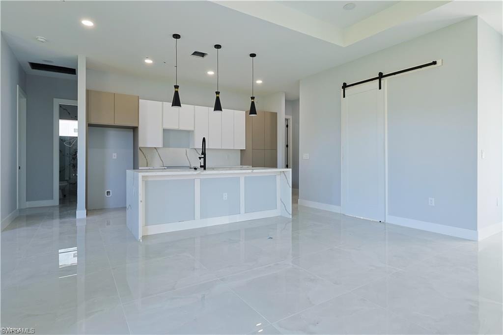 Kitchen featuring a barn door, modern cabinets, an island with sink, decorative light fixtures, and recessed lighting