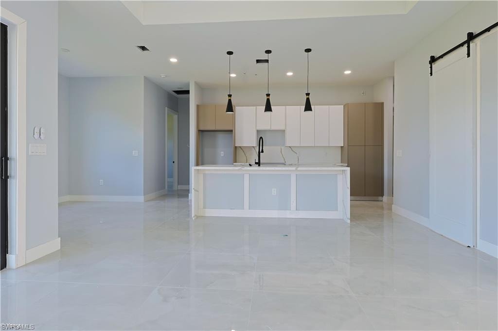 Kitchen featuring a barn door, modern cabinets, decorative light fixtures, a center island with sink, and recessed lighting