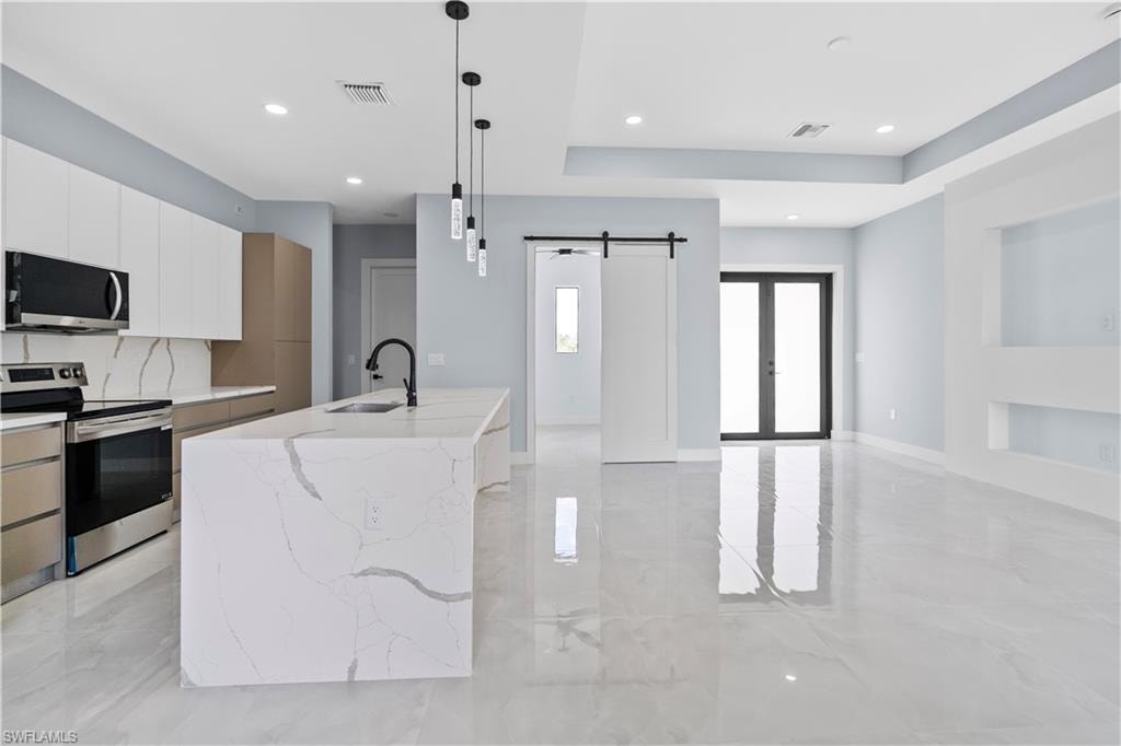 Dual tone kitchen with stainless steel appliances, light stone counters, a barn door, dual tone cabinetry, and hanging light fixtures